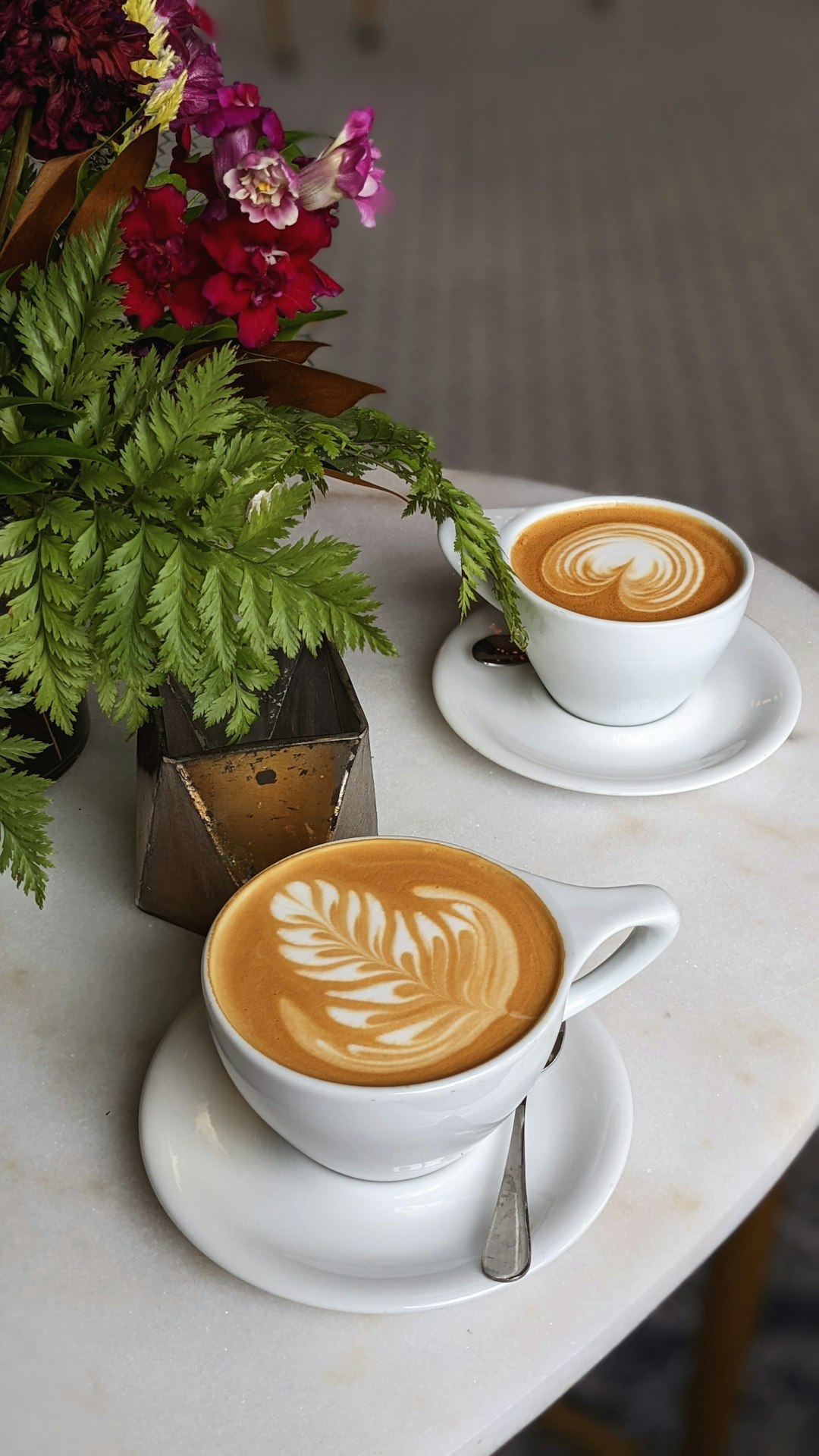 two cups of coffee on a table with a vase of flowers